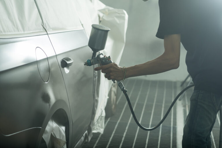 Auto body repair series: Worker painting black car in paint booth