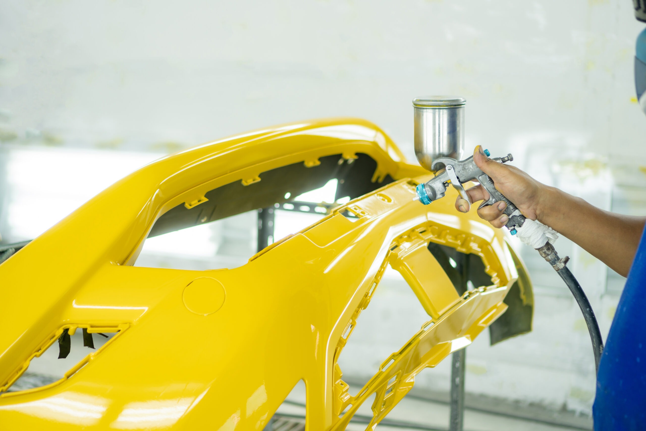 Man with protective clothes and mask painting car using spray compressor ,yellow front bumper