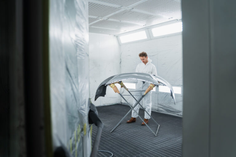 Auto paint master restores car bumper. Male worker of a auto body workshop in a vehicle painting booth